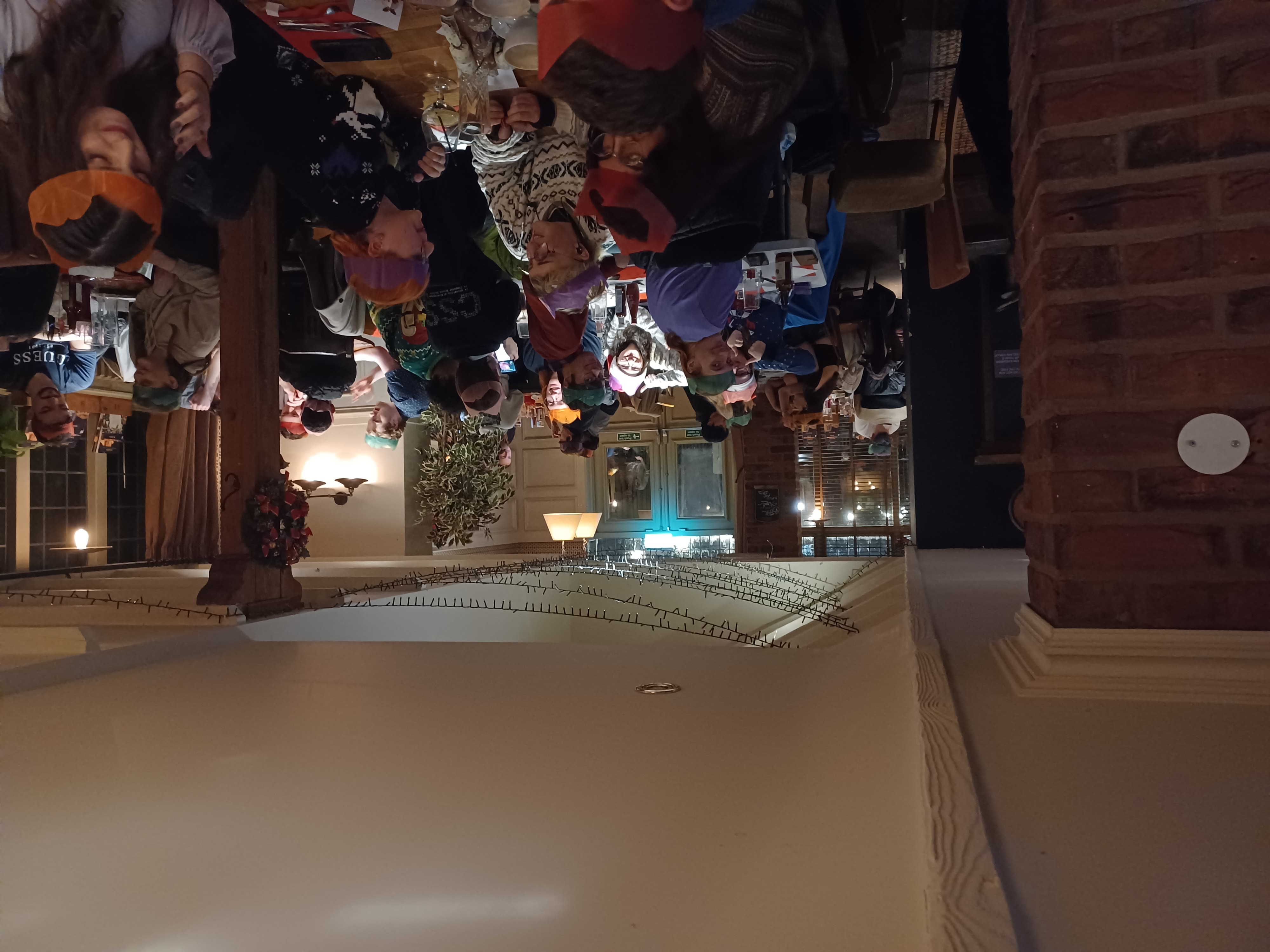 A photo at the Christmas Meal, inside of the Green Man. Students and members are sat around tables, enjoying their food or talking amongst themselves.
